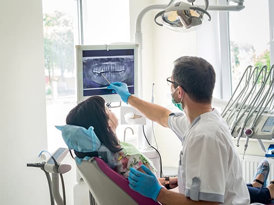 Dentist showing a patient their dental X-ray on a screen during a consultation in a brightly lit dental office.