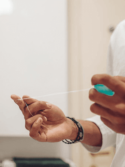 Person holding dental floss between their fingers, wearing a bracelet, in a bathroom setting.